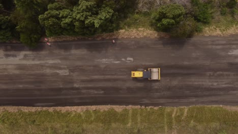 aerial top down view of road roller, leveling sand and gravel during countryside road construction