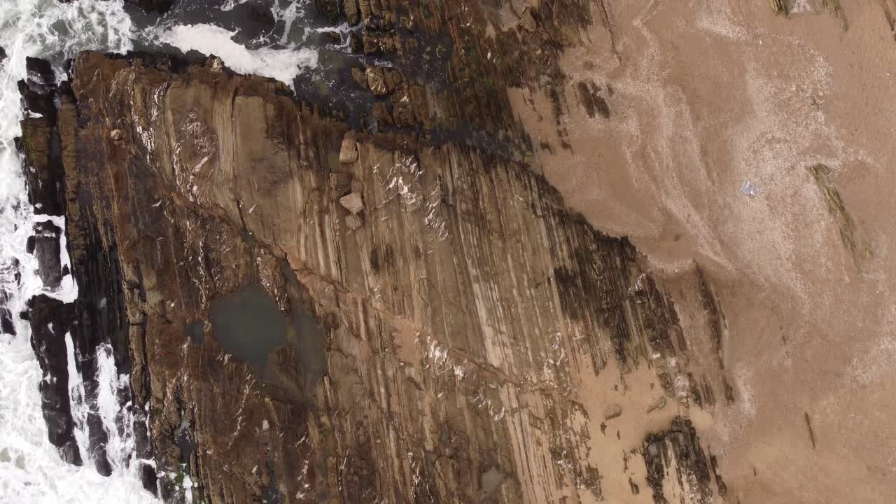 toma aérea de pájaros de olas que inundan espectaculares rocas antiguas - hermosa textura de patrón desde arriba - la pedrera, uruguay
