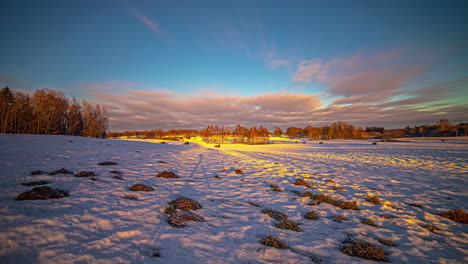 orange clouds in golden sky over snowy landscape with trees in a winter time-lapse