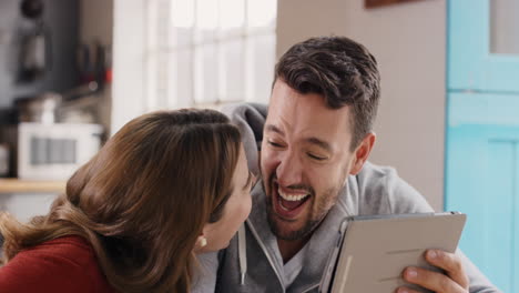 Attractive-young-couple-at-home-laughing-at-funny-internet-joke-online-using-digital-tablet