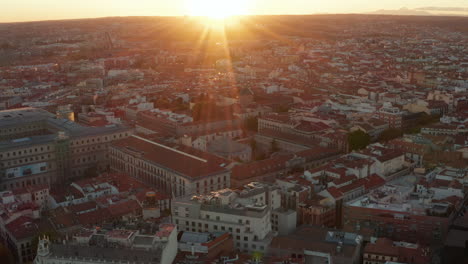 Aerial-shot-of-buildings-in-town-centre.-Tilt-up-reveal-cityscape-and-setting-sun-on-horizon.