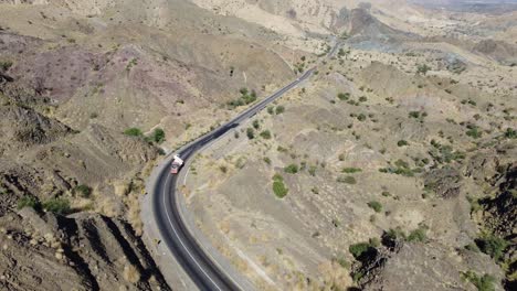 aerial drone forward moving shot over cars and trucks moving on a winding rcd road through balochistan on a sunny day