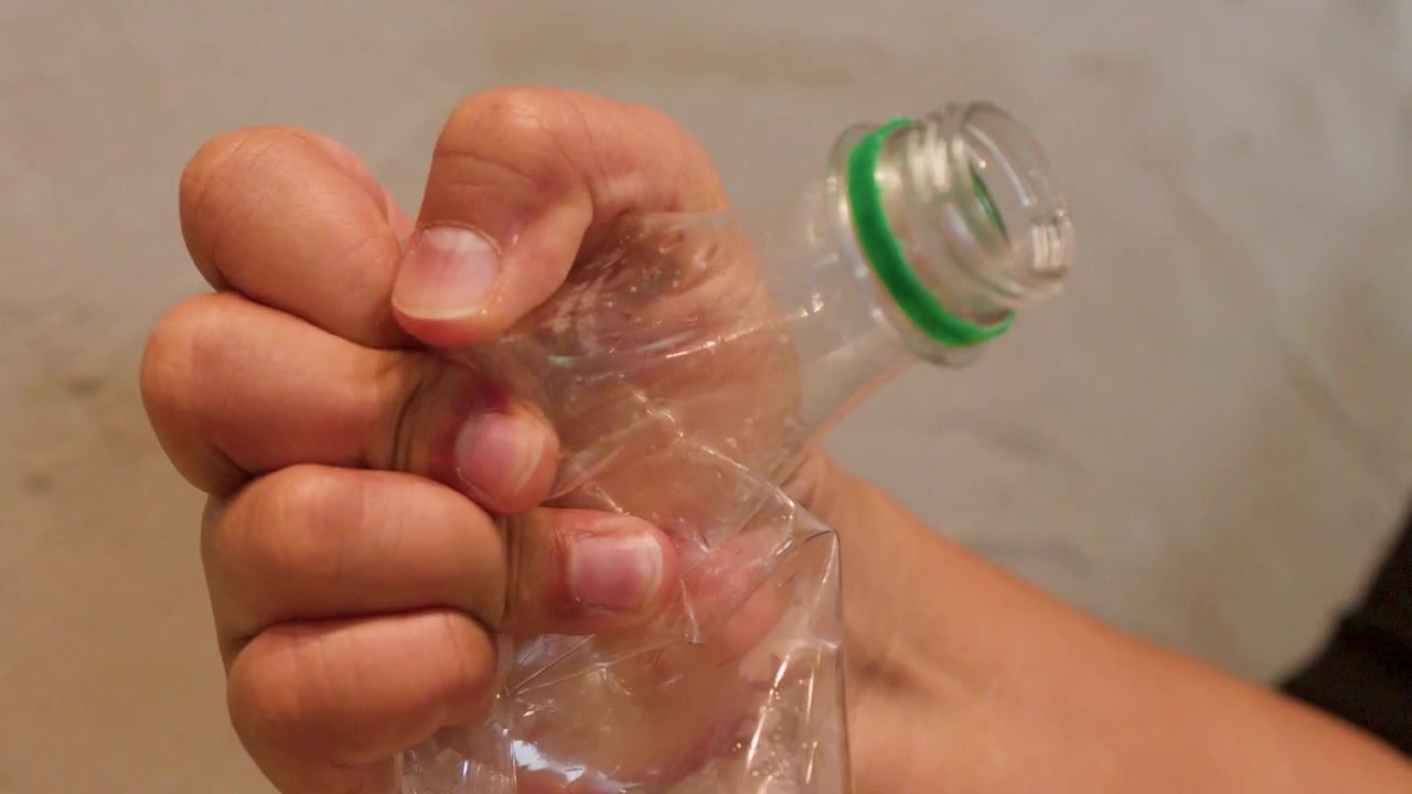 Un primo piano mostra una mano asiatica che schiaccia una bottiglia d'acqua di plastica trasparente per il riciclo