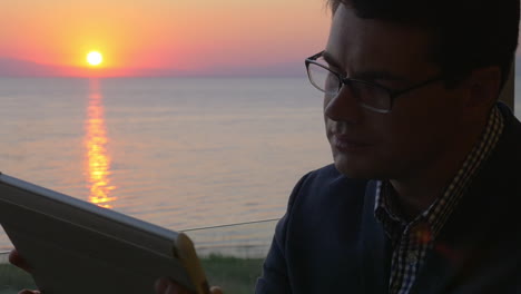 Man-working-with-pad-on-the-balcony-at-sunset