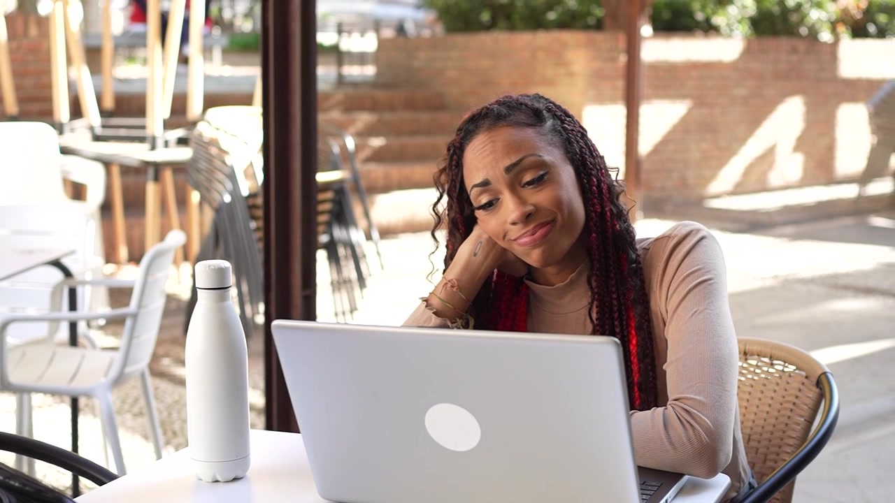 A stressed woman is working on her laptop at a cafe facing multiple challenges today