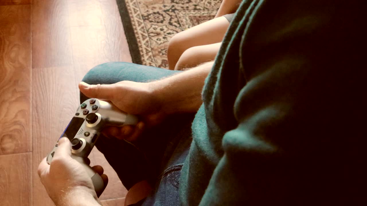 un video 4k usando un controller per giocare a videogiochi - un primo piano di mani e un joystick, un giovane che gioca, e suo figlio seduto accanto a lui