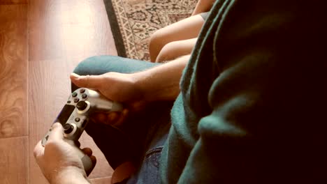 un video de 4k usando un controlador para jugar videojuegos - un primer plano de manos y un joystick, un joven jugando, y su hijo sentado a su lado