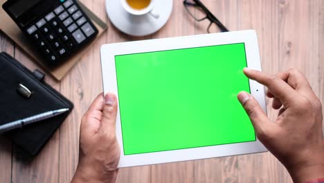 persona usando una tableta con una pantalla verde en una mesa de madera
