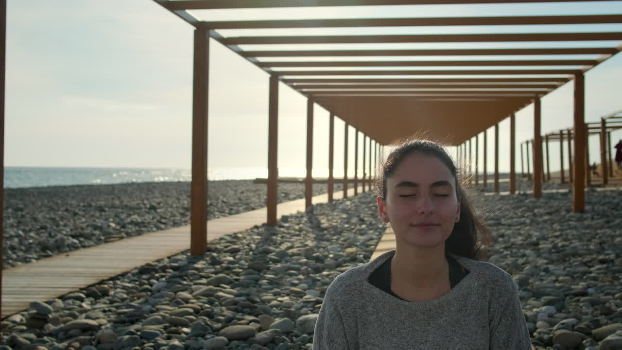mujer meditando en una playa con pasarela de madera y pérgola
