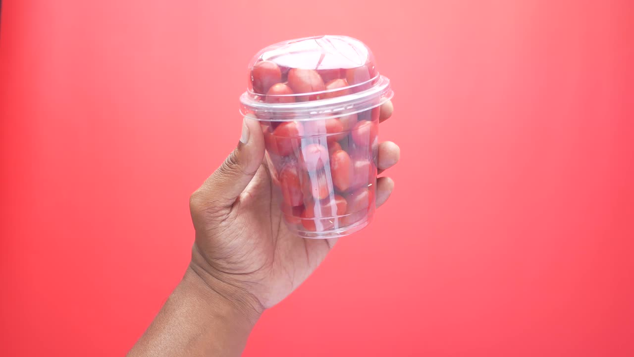 mano sosteniendo una taza de plástico transparente de tomates cereza