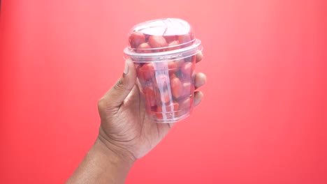 mano sosteniendo una taza de plástico transparente de tomates cereza