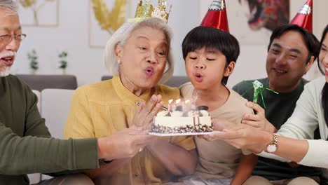 an elderly asian family joyfully celebrates a birthday, blowing out candles on a cake in a warm, festive setting