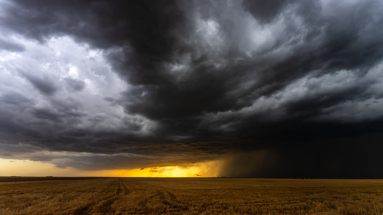Warm sunset light below dark storm clouds moving across fields