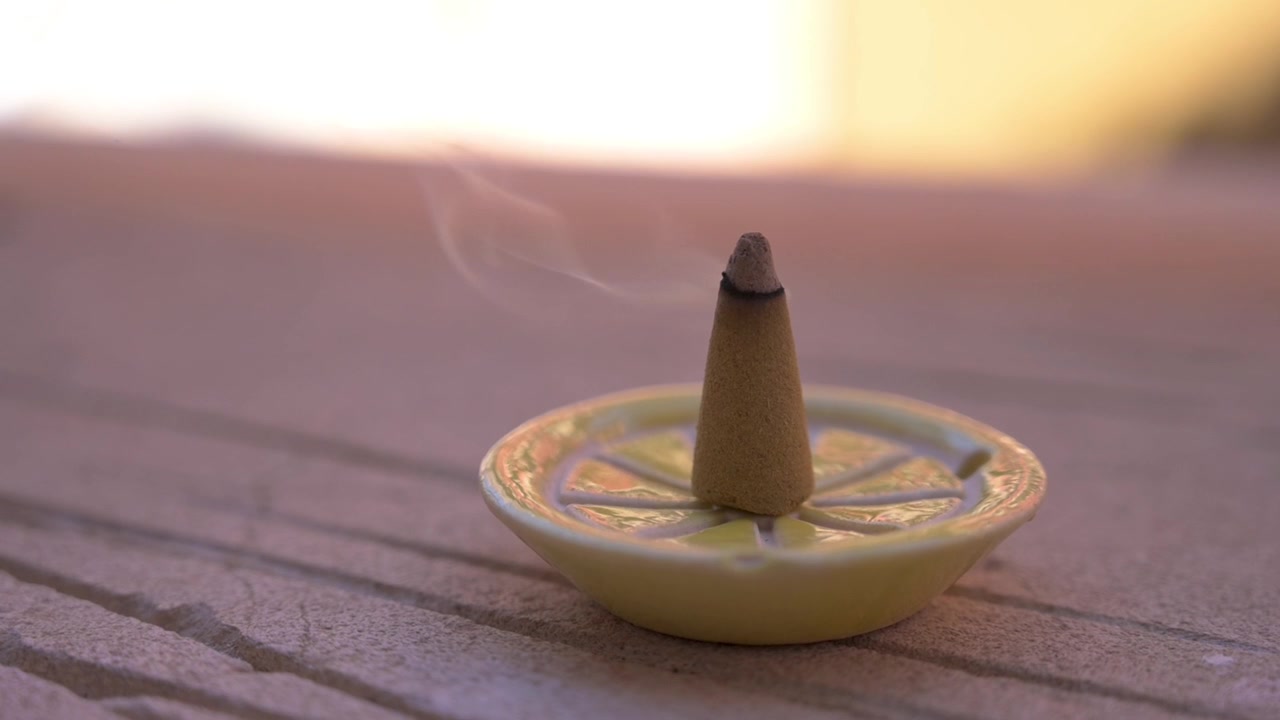 Bastoncino d'incenso alla citronella a forma di cono che fuma delicatamente in un porta incenso in ceramica su una sporgenza di pietra