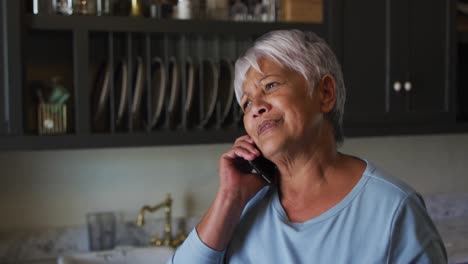 Feliz-Mujer-De-Raza-Mixta-Senior-Hablando-Por-Teléfono-Inteligente-En-La-Cocina