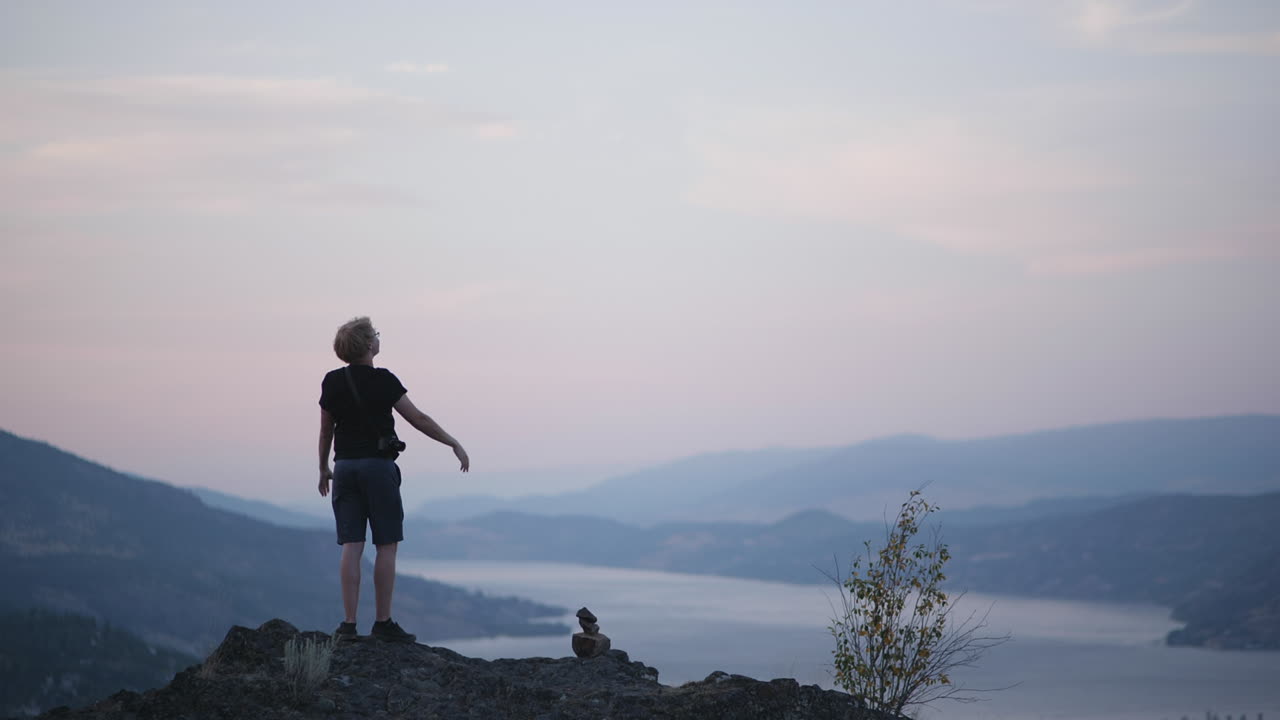 Hiker stands with arms raised on mountaintop with beautiful sunset view