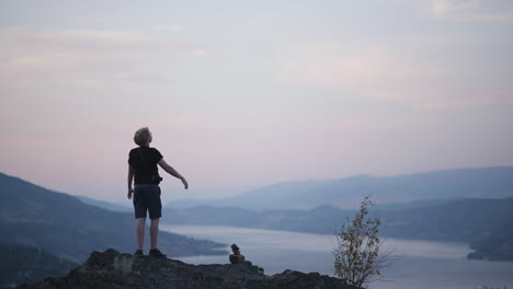 hiker stands with arms raised on mountaintop with beautiful sunset view