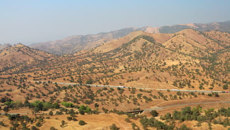 Long-straight-highway-cutting-through-the-dry,-southern-California-grasslands---aerial-view