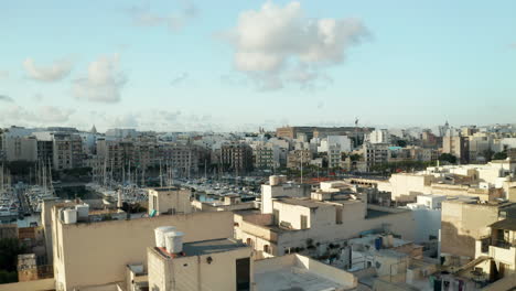 Dolly-forward-over-Roof-Terrace-revealing-Port-of-Mediterranean-City-Town-on-Malta-Island-in-Brown-Beige-and-Blue-Color,-Aerial-View