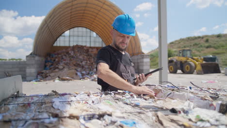 trabajador masculino con una tableta chequea las balas de papel en la planta de reciclaje al aire libre