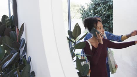 feliz pareja de lesbianas biraciales llegando a casa y hablando en el teléfono inteligente, en cámara lenta