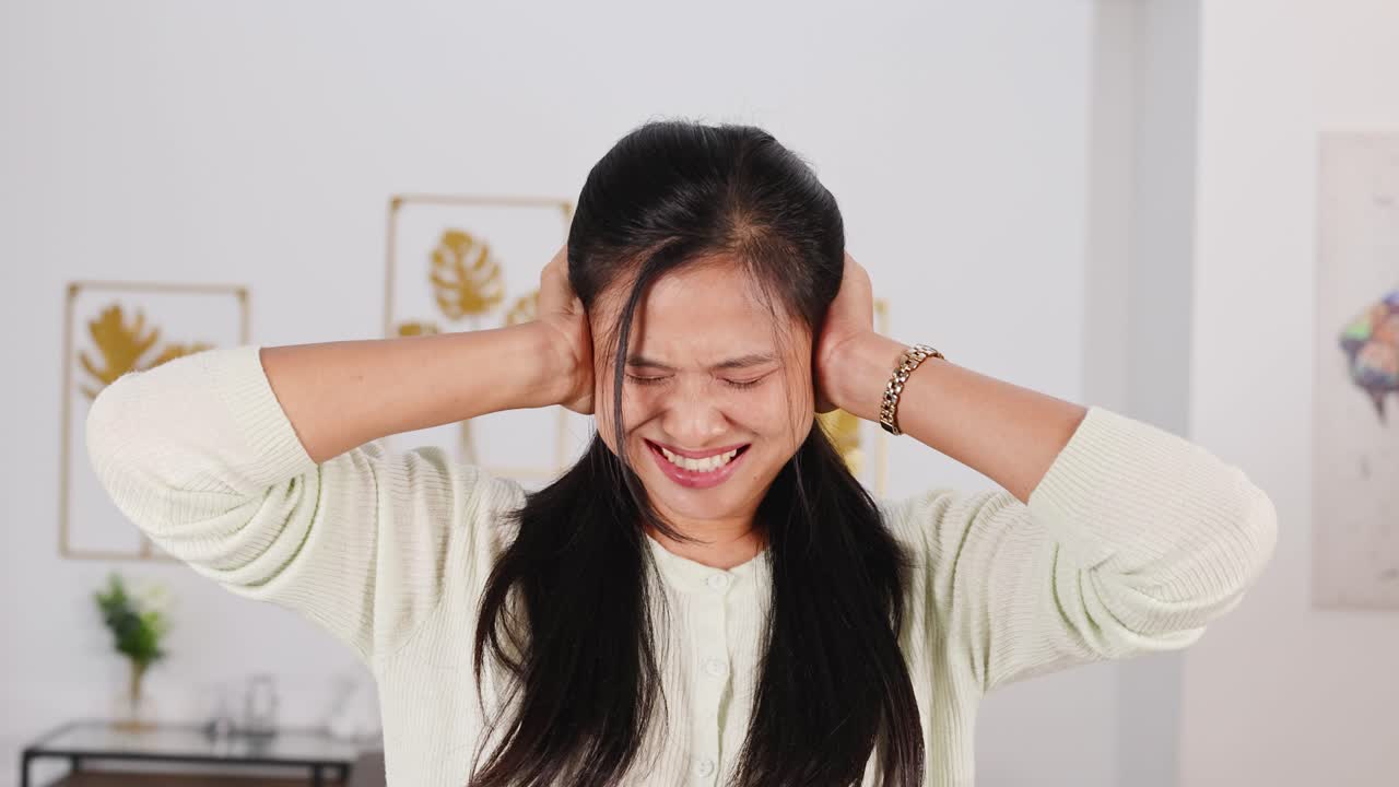 A woman covers her ears, showing frustration or stress, in a well-lit room with decorative elements