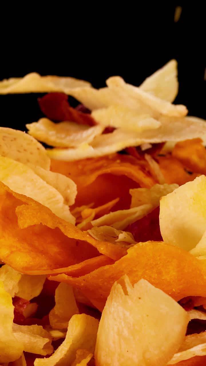 Colorful root vegetable chips fall and scatter in slow motion, isolated on a black background