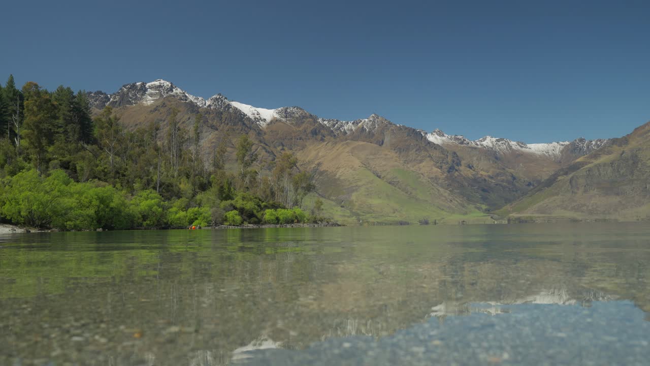 aguas tranquilas y claras de la bahía de wilson con altas montañas en el fondo, nueva zelanda
