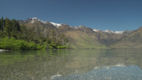 Calm-clear-water-of-Wilson-bay-with-tall-mountains-in-background,-New-Zealand