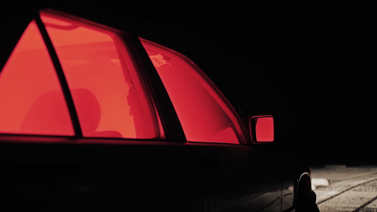 Stylized nighttime shot of a parked car with glowing red windows with smoke inside, evoking a cinematic crime-thriller mood