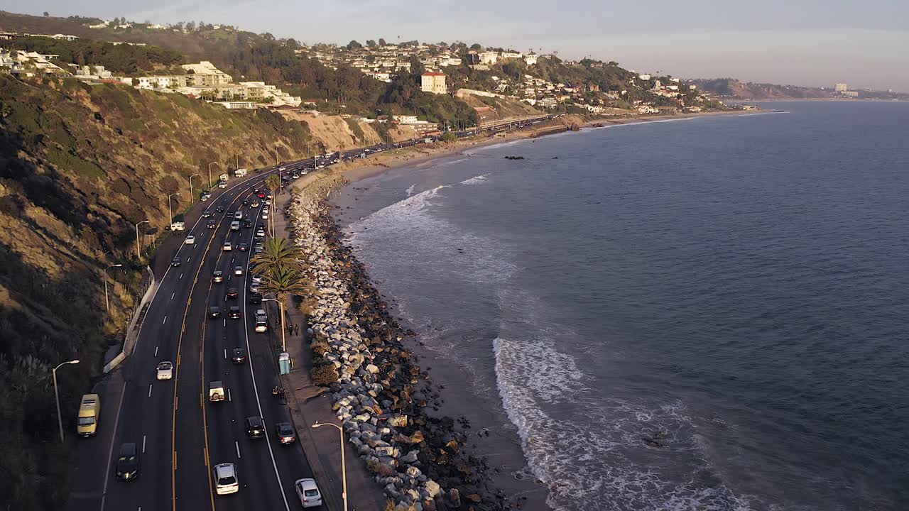 Cinematic aerial view of Late afternoon traffic on California State Route one with Pacific Coastline and surrounding nature.