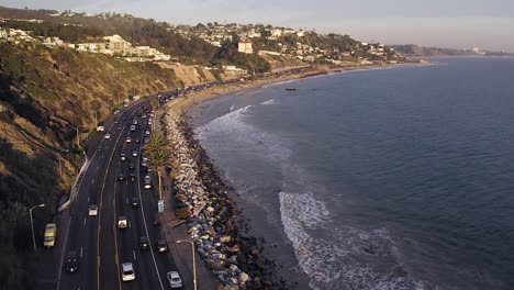 cinematic aerial view of late afternoon traffic on california state route one with pacific coastline and surrounding nature.