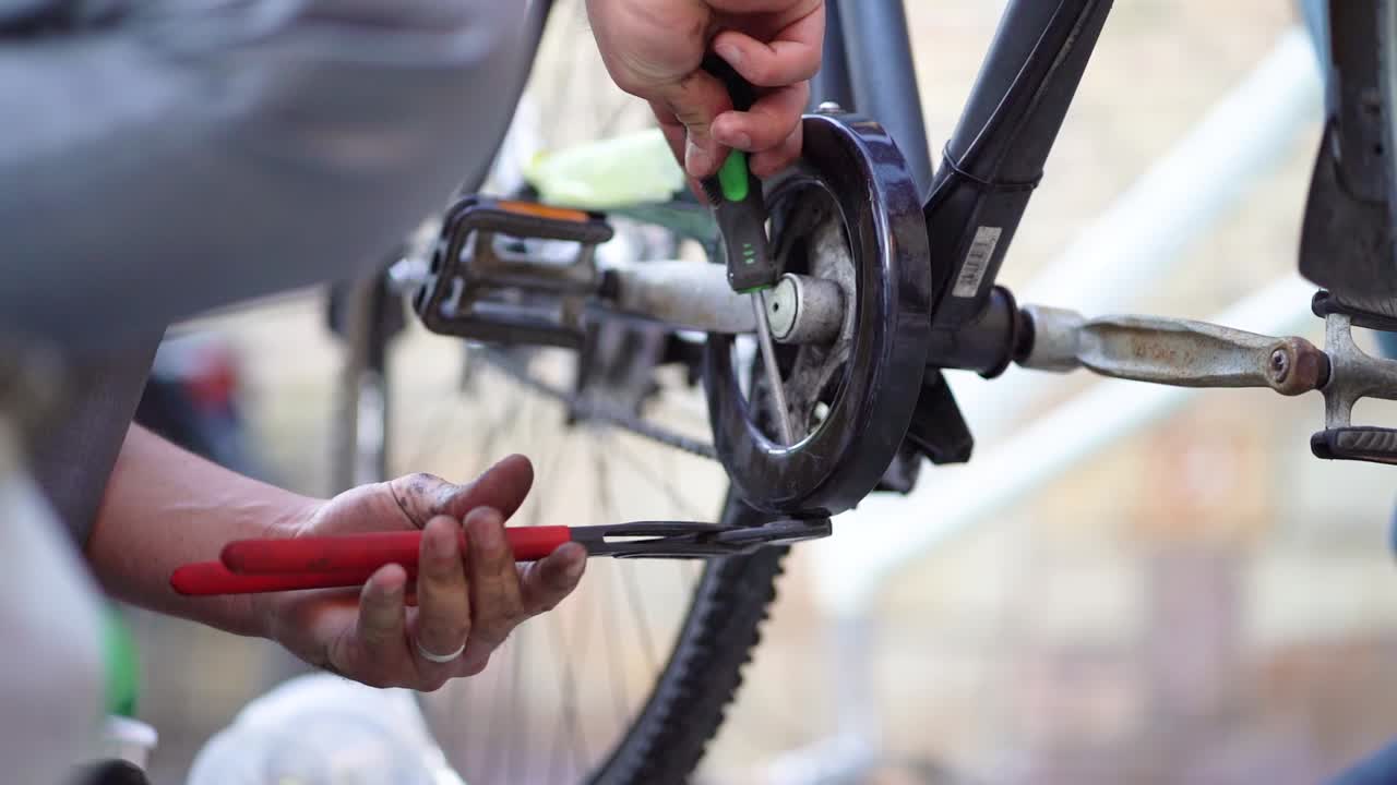 Caucasian male mechanic strong hands use screwdriver and wrench to tighten screw on bicycle pedal, close up static