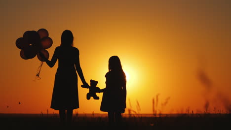 Mom-And-Daughter-Admire-The-Sunset-Hold-Balloons-And-A-Teddy-Bear