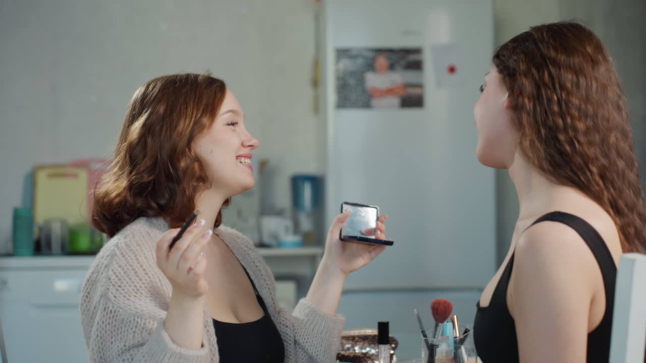 Two White Women Laughing While Applying Makeup, Informal Kitchen Setup, Palette Exchange And Mirror Checking, Playful Lesson Vibe, Friendly Teaching Moment, Candid Gestures And Shared Smiles