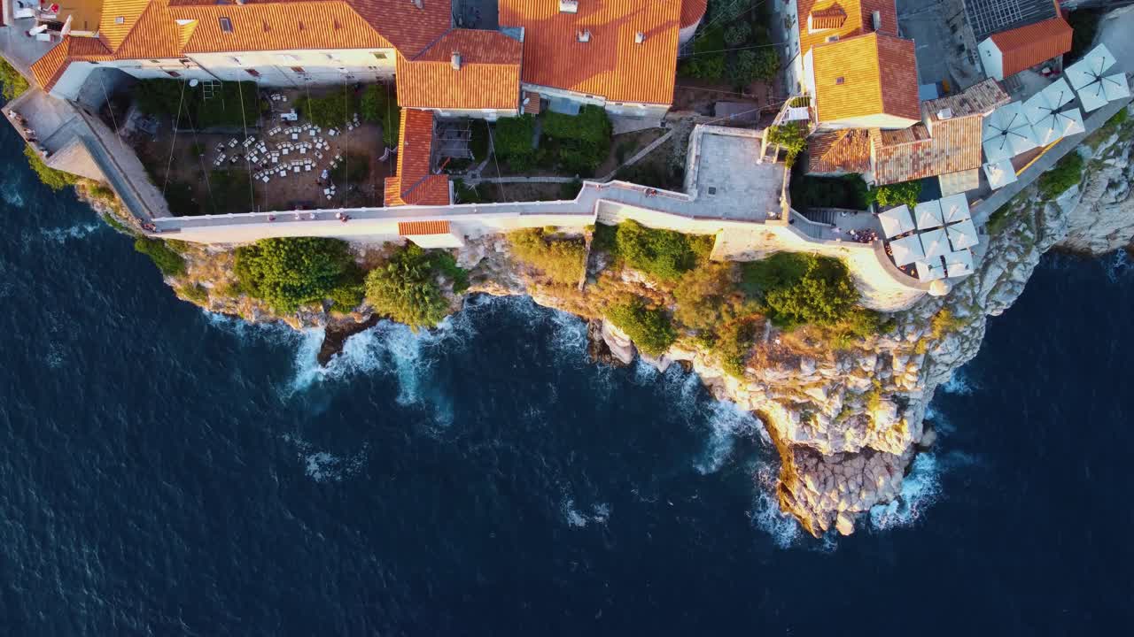 Vista aérea cenital en Dubrovnik, Croacia, de olas rompiendo contra los acantilados debajo de las murallas de la ciudad al atardecer