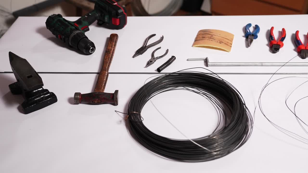 Ståltrådsspole, ambolt, hammer, tang og boremaskine arrangeret på et bord til traditionelt slovakisk trådhåndværk. Drotarstvo værkstedsforberedelse med værktøj og materialer til håndlavet metalkunst.