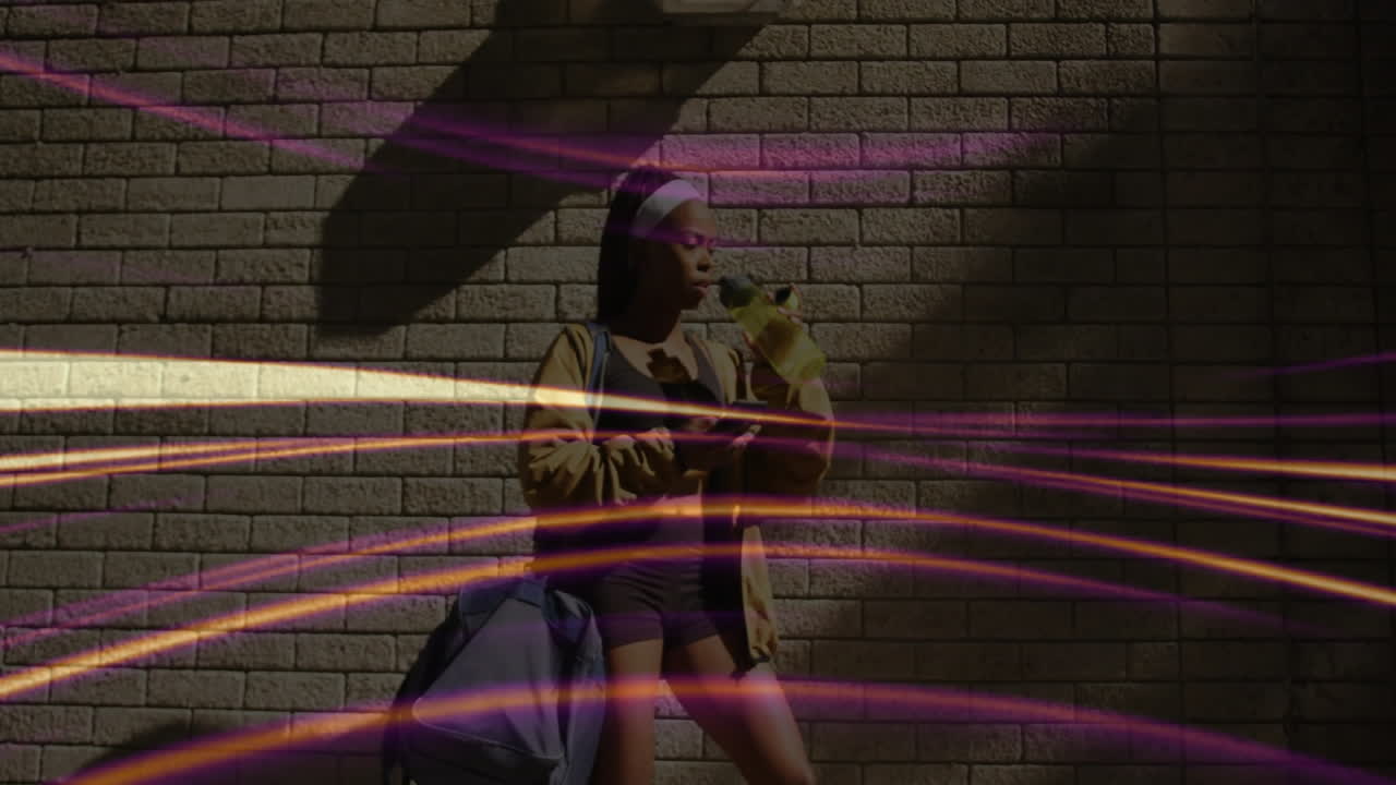Woman drinking water and checking fitness app on phone against brick wall, showing animated streaks