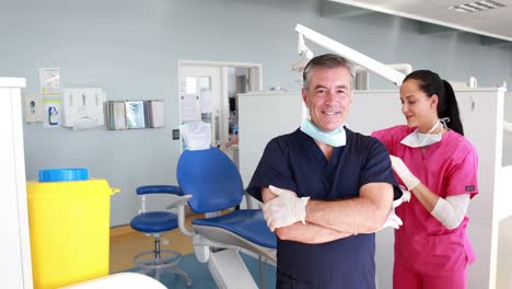 Smiling-dentist-with-arms-crossed-in-front-of-his-assistant