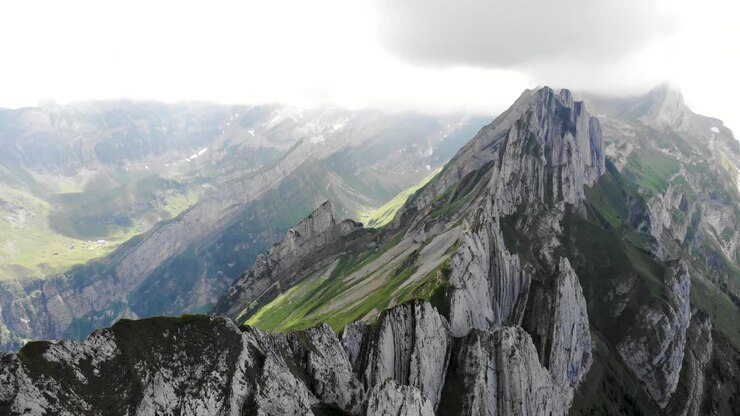 Aerial flyover over the cliffs of Schafler ridge in Appenzell, Switzerland with pan down camera motiion revealing the cliffs and hiking trail above the lush green mountain slope