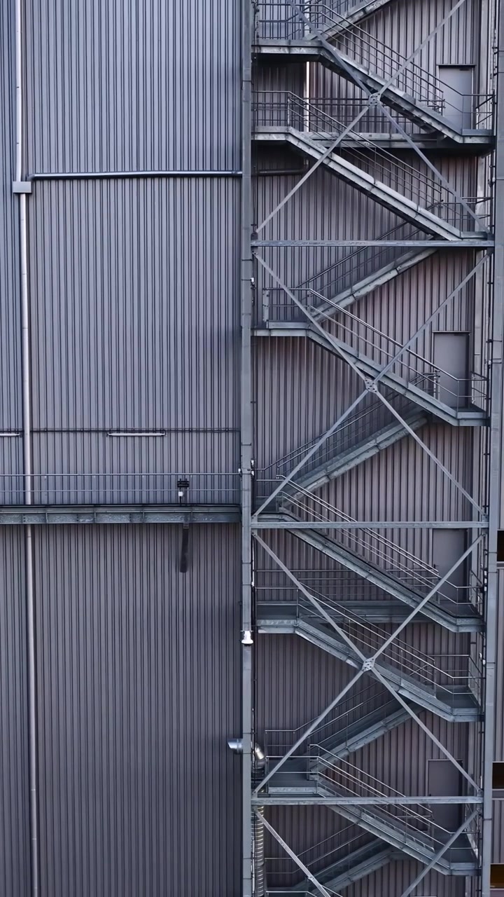 Una vista verticale di un edificio industriale rivestito in metallo, caratterizzato da una scala esterna prominente e tubature. Adatto per studi di architettura e progetti di design industriale.
