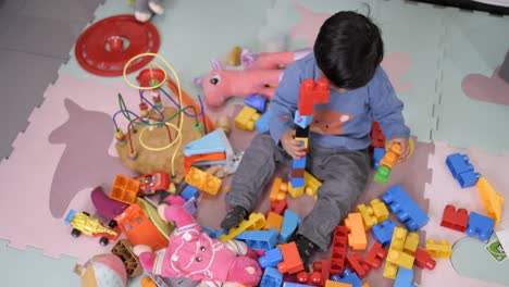 two years old mexican baby boy playing with didactic toys on messy floor