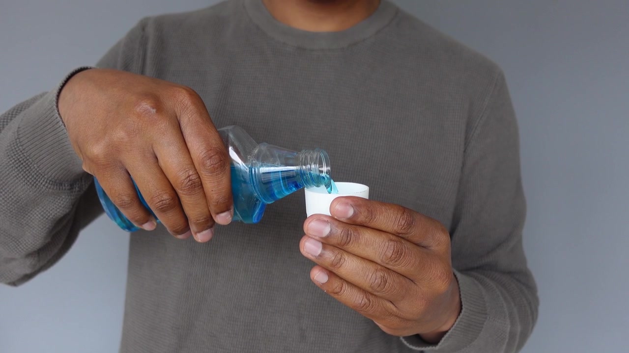 Hombre vertiendo enjuague bucal azul en una taza pequeña para la higiene bucal