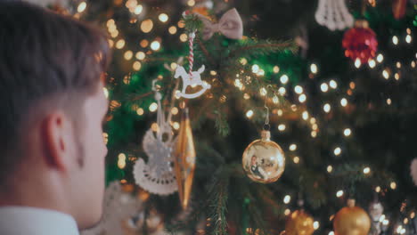 man hand hanging golden shiny bauble on illuminated christmas tree