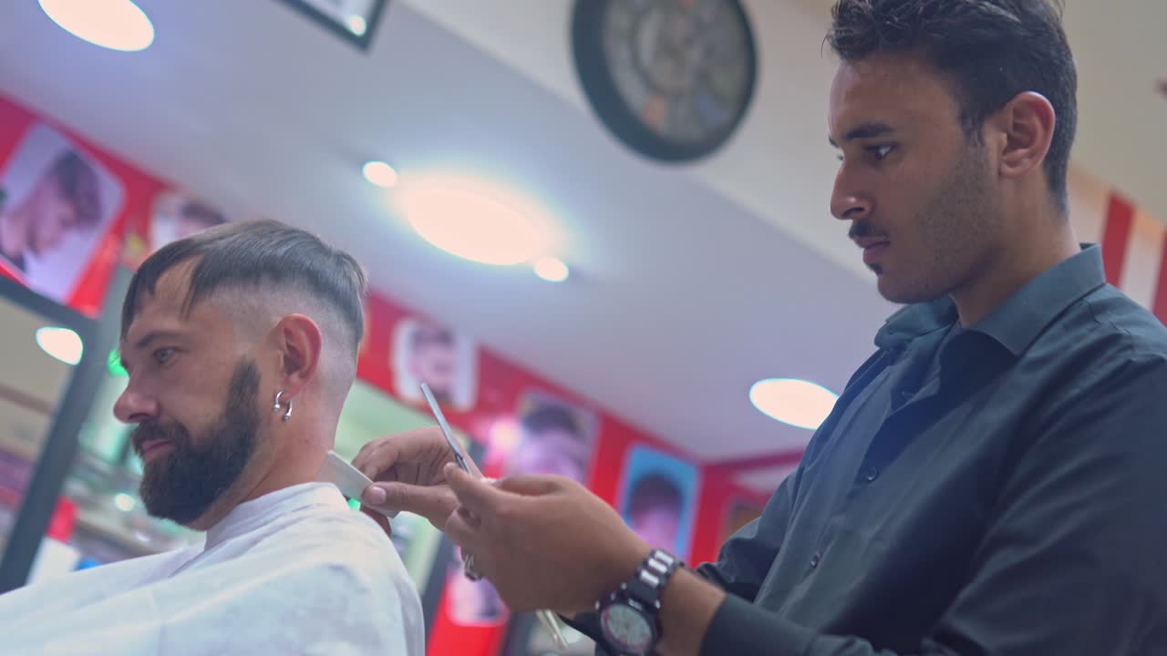Barbiere che taglia i capelli a un uomo con un rasoio a mano libera in una barberia.