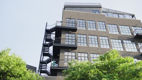 Warehouse-lofts-of-brown-brick,-renovated-with-large-bay-windows-and-black-steel-fire-escape-stairwells,-breathe-new-life-into-the-cityscape