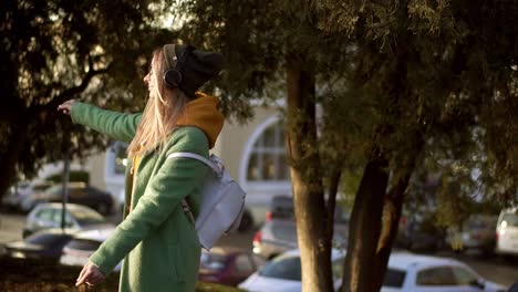 Blonde-woman-dance-in-winter-park,-listening-to-music-on-the-phone-using-headphones,-spinning-around