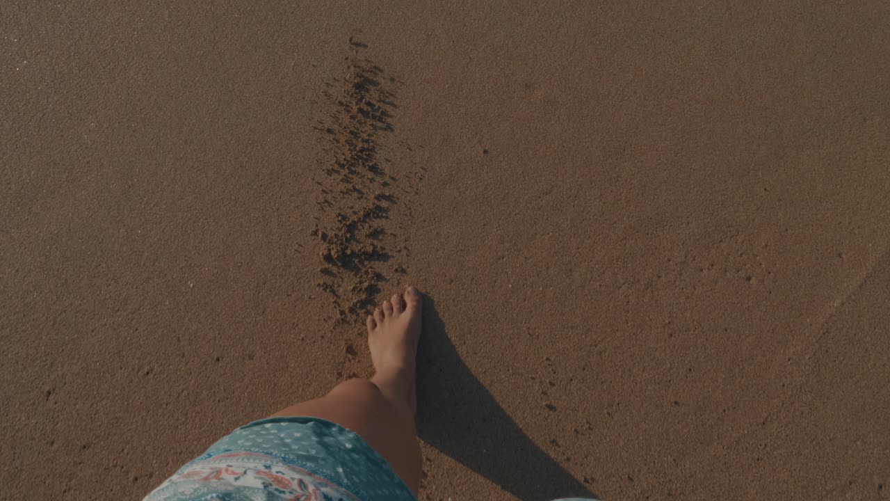 A Girl with beautiful legs walking over the beach towards the sea until the water touches her feet