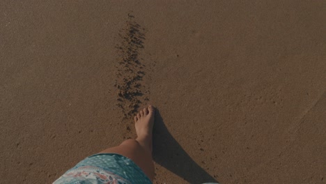 a girl with beautiful legs walking over the beach towards the sea until the water touches her feet