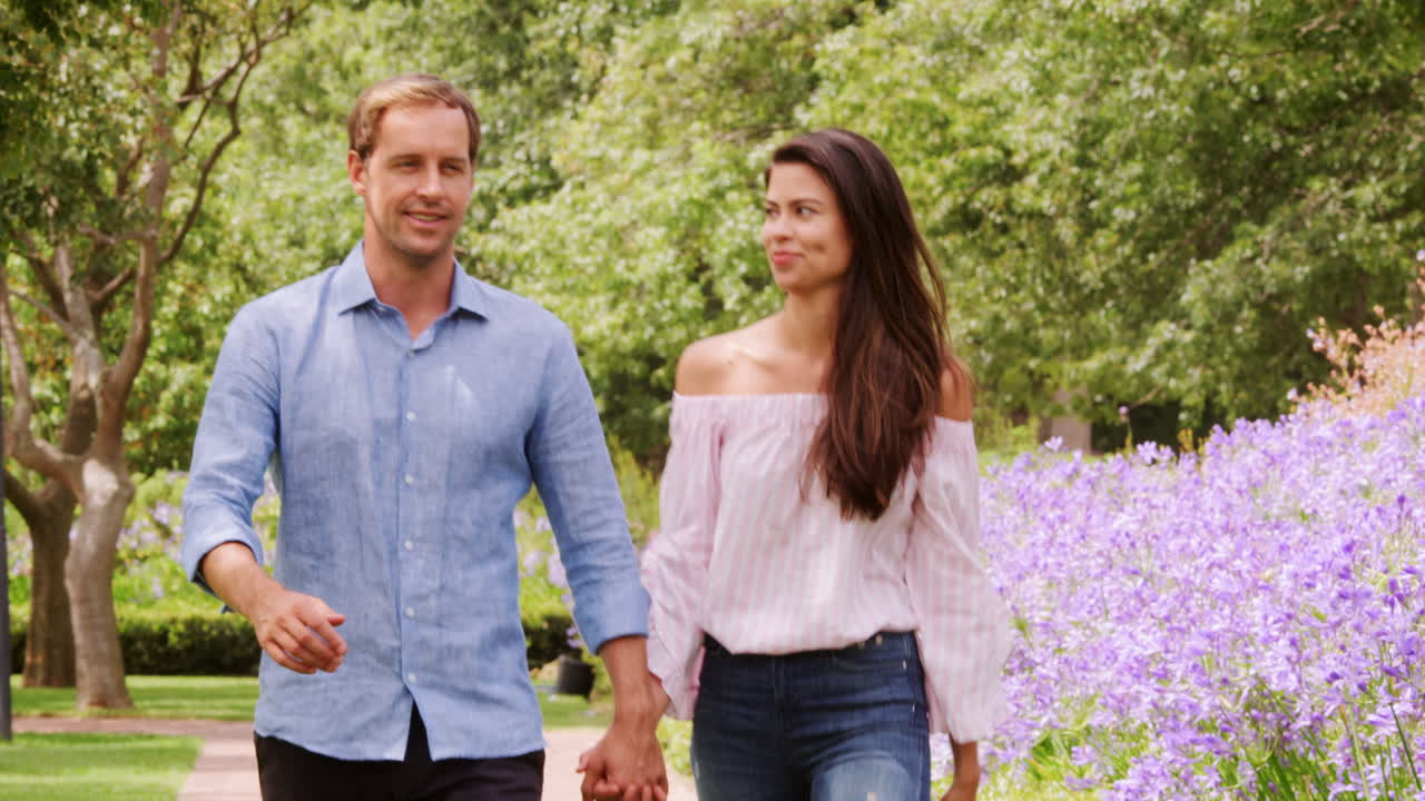 젊은 백인 커플이 공원을 가로질러 손잡고 고 있다